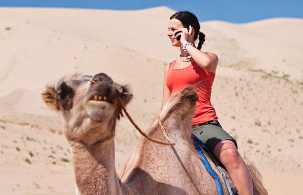 woman on phone while riding camel